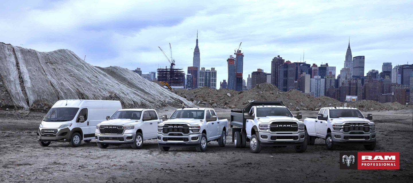 Línea de la marca Ram 2025 toda en blanco, con los vehículos estacionados uno al lado del otro en una obra de construcción, con un paisaje urbano de fondo. De izquierda a derecha: una Ram ProMaster 3500 SLT High Roof Cargo Van, una Ram 1500 Tradesman 4x4 Crew Cab, una Ram 2500 Tradesman 4x4 Crew Cab 2024, una Ram 5500 Tradesman Chassis Regular Cab 2024 con mejoras de carrocería volcadora y una Ram 3500 Tradesman 4x4 Crew Cab 2024. Ram Profesional.