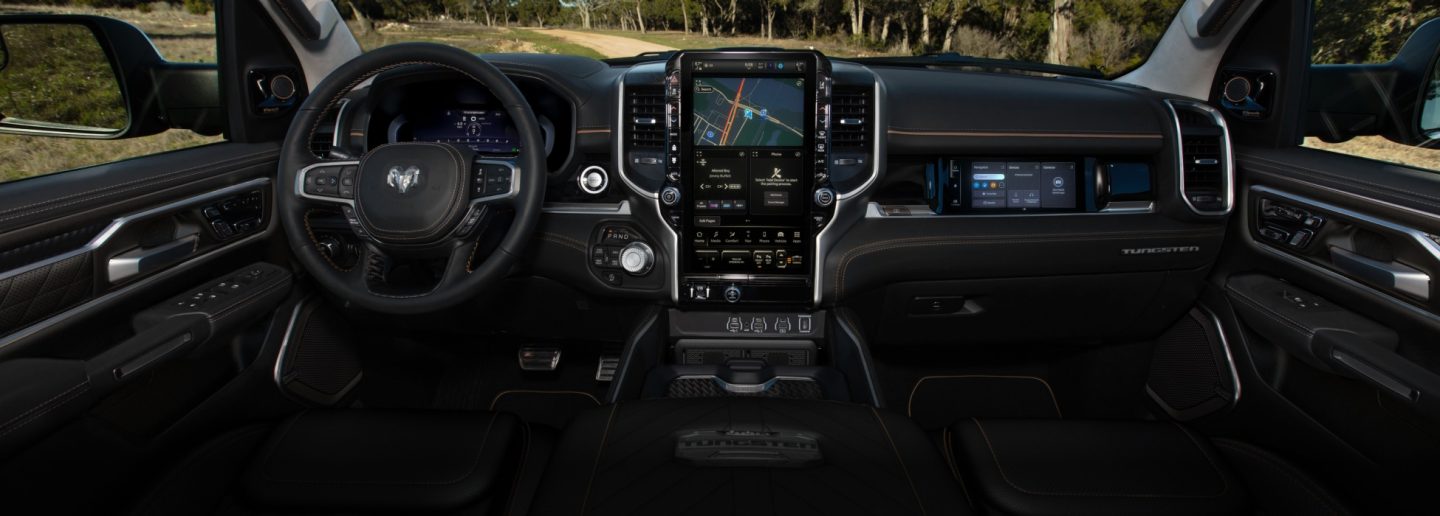 The front seat area in the 2026 Ram 1500 Tungsten, highlighting the steering wheel, Digital Cluster Display, Uconnect touchscreen and Front Passenger Interactive Display.