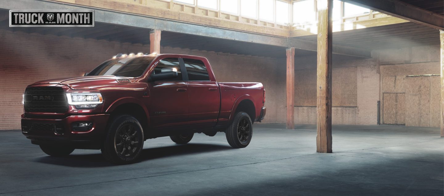 A red 2022 Ram 2500 Limited 4x4 Crew Cab with its headlamps on, parked in a commercial garage. The Ram Truck Month logo.