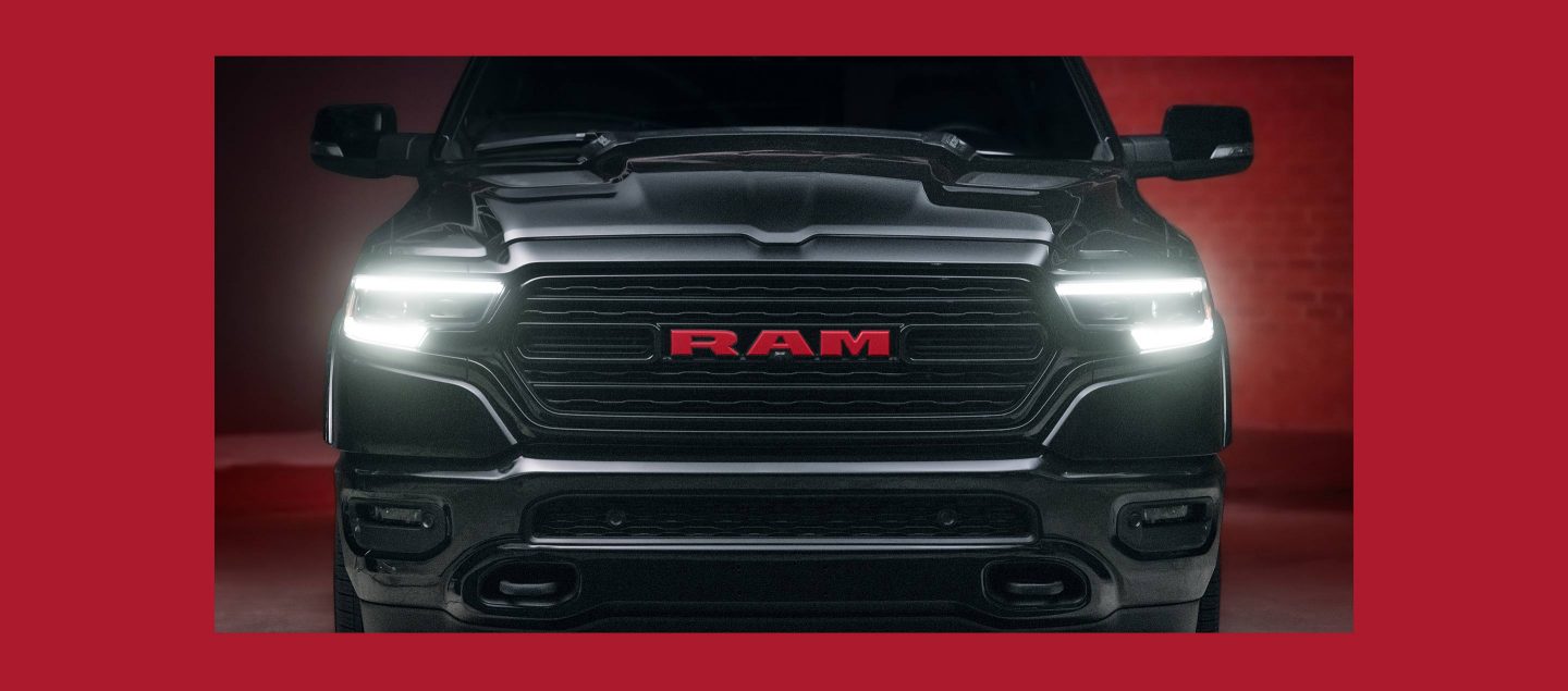 A close-up of the front end of a 2023 Ram 1500 Limited Ram Red Edition with its headlamps on.