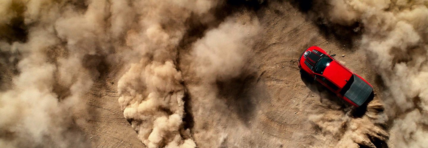 An overhead view of a red 2021 Ram 1500 TRX creating doughnuts in the sand, kicking up clouds of dust.