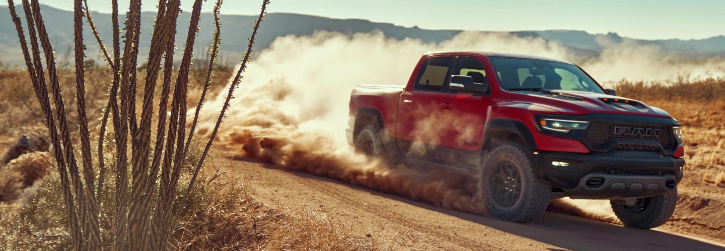 The 2022 Ram TRX being driven on a dirt road with dust clouds rising from its wheels.