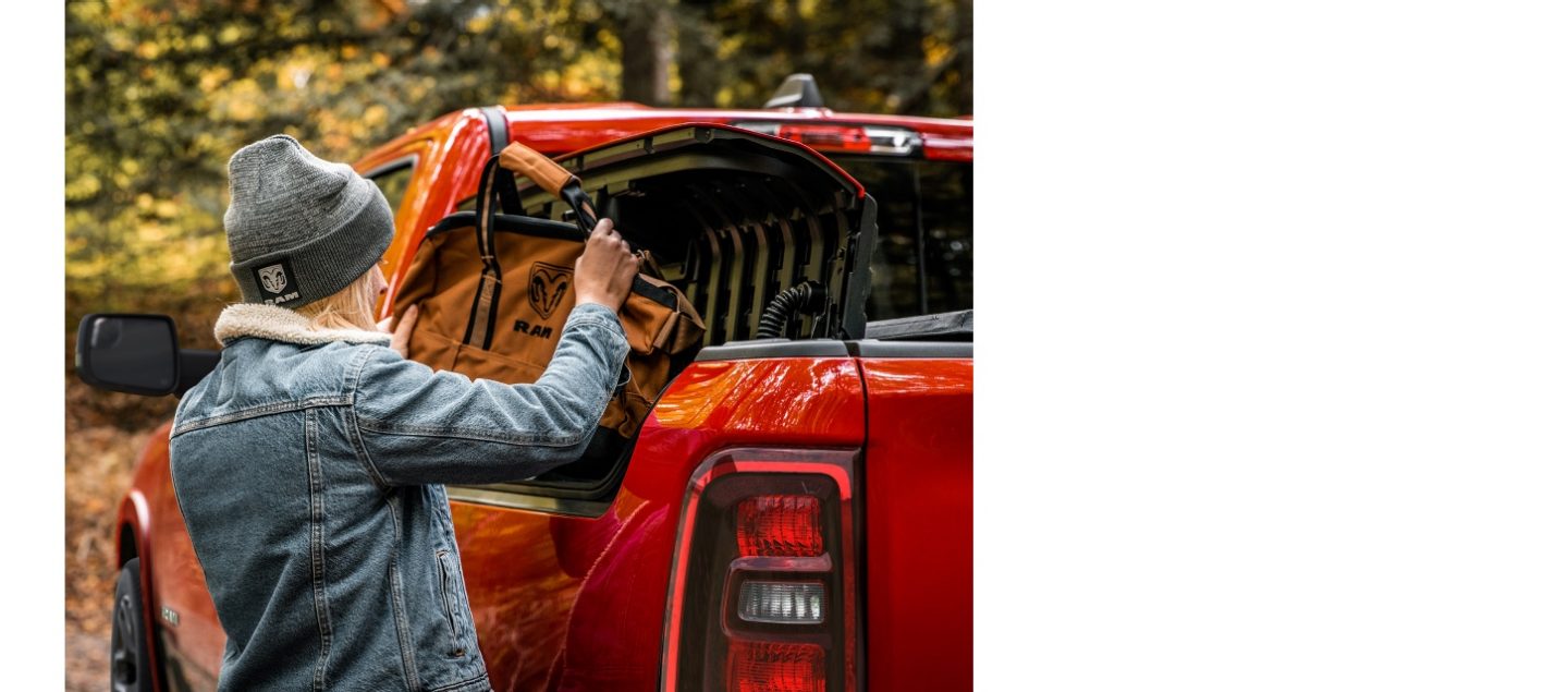 A person taking a Ram Brand duffle bag out of the Ram Box on a red Ram 1500 Laramie 4x4 Crew Cab.