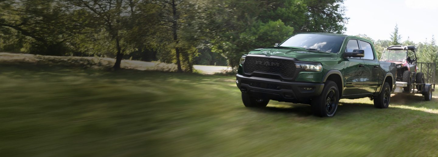 Una Ram 1500 Rebel 4x4 Crew Cab 2026 verde remolcando un ATV sobre un remolque utilitario.