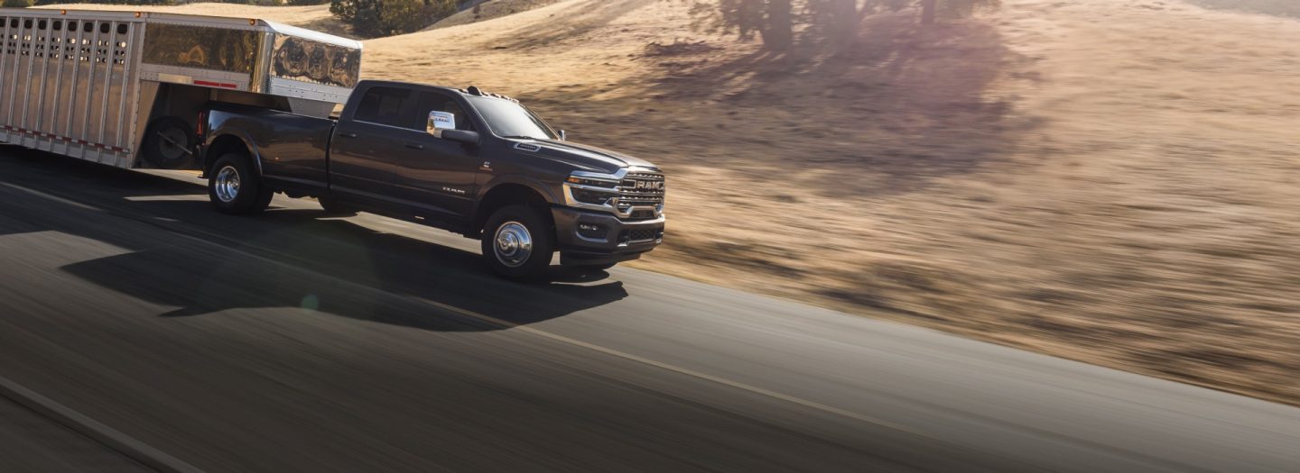 Una Ram 3500 Limited Longhorn Crew Cab 2026 negra llevando un gran remolque ganadero de quinta rueda mientras avanza por una carretera.