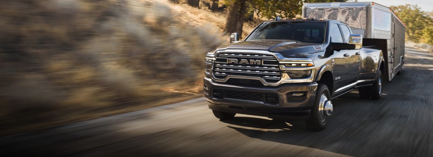 Una Ram 3500 Limited Longhorn 4x4 Crew Cab 2026 gris acarreando un remolque de quinta rueda grande para ganado mientras circula por una carretera. El fondo está borroso para indicar que la camioneta está en movimiento.