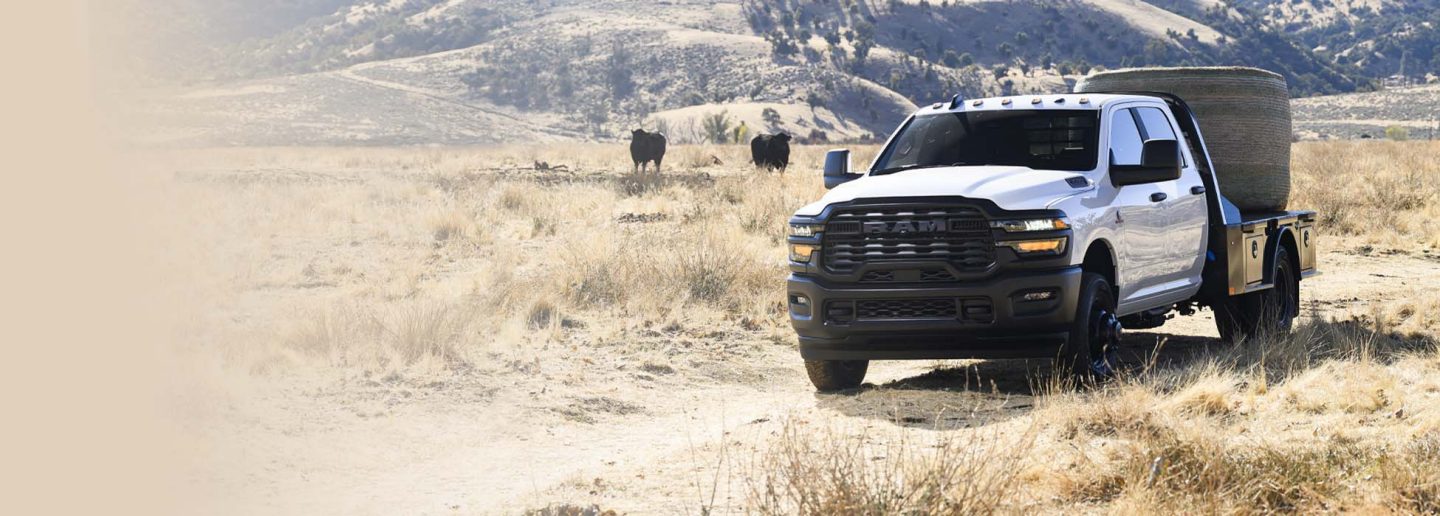 Una Ram 3500 Tradesman 4x2 Chassis Cab Crew Cab 2026 blanca, estacionada en un rancho ganadero, carga un fardo de heno en su caja tipo plataforma.