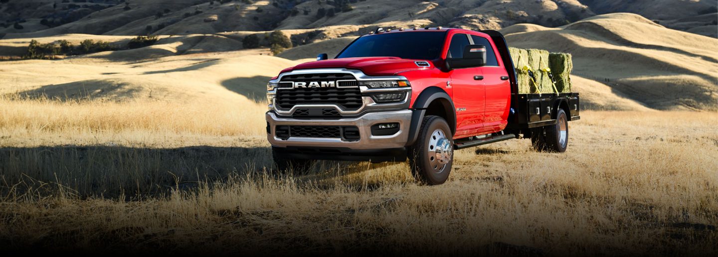 Una Ram 5500 Laramie Chassis Crew Cab 2026 roja transportando varios fardos de heno grandes sobre una mejora de plataforma larga.