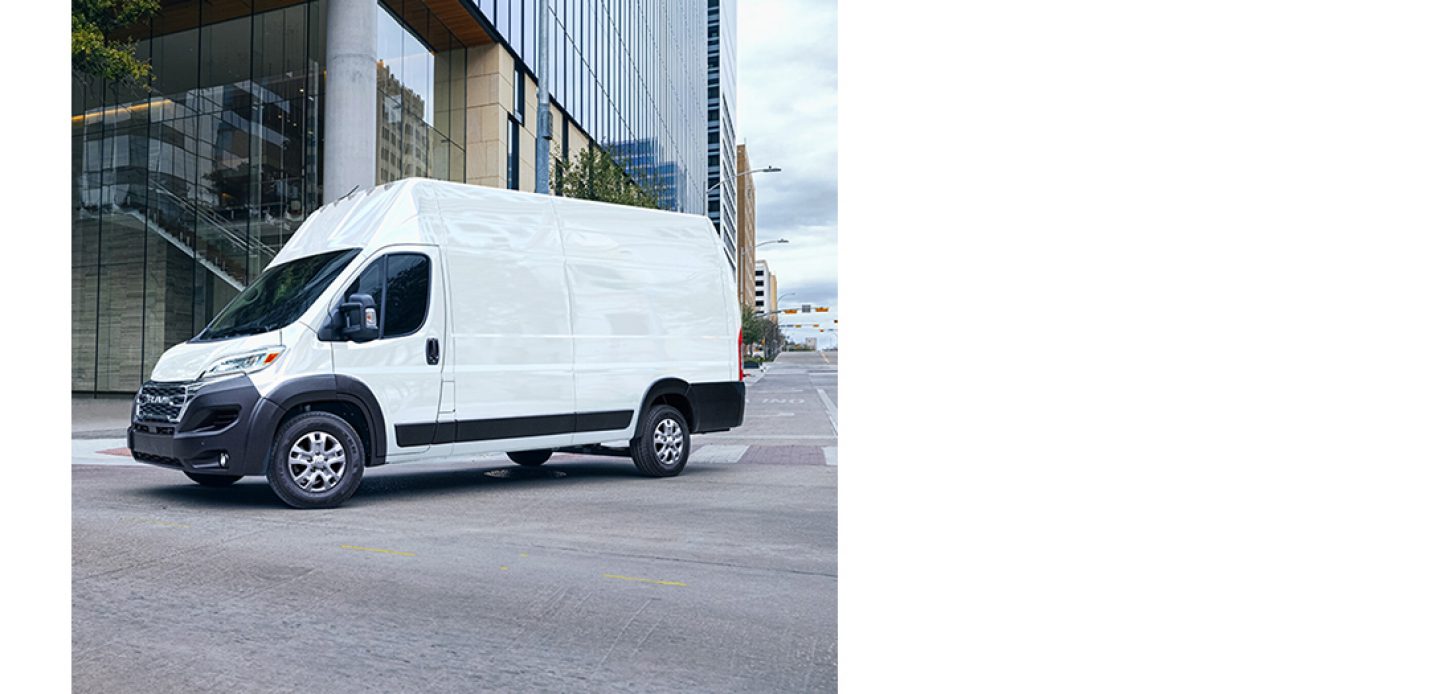 Una furgoneta Ram ProMaster 3500 SLT Plus Cargo Van Super High Roof blanca del año 2026 girando a la derecha en un cruce con semáforo en una calle de la ciudad.