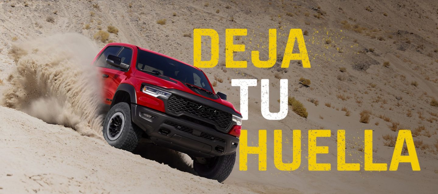 Una Ram 1500 RHO 4x4 Crew Cab 2027 roja, fotografiada mientras desciende una duna en ángulo, levantando arena a su paso. Reclama tu derecho.