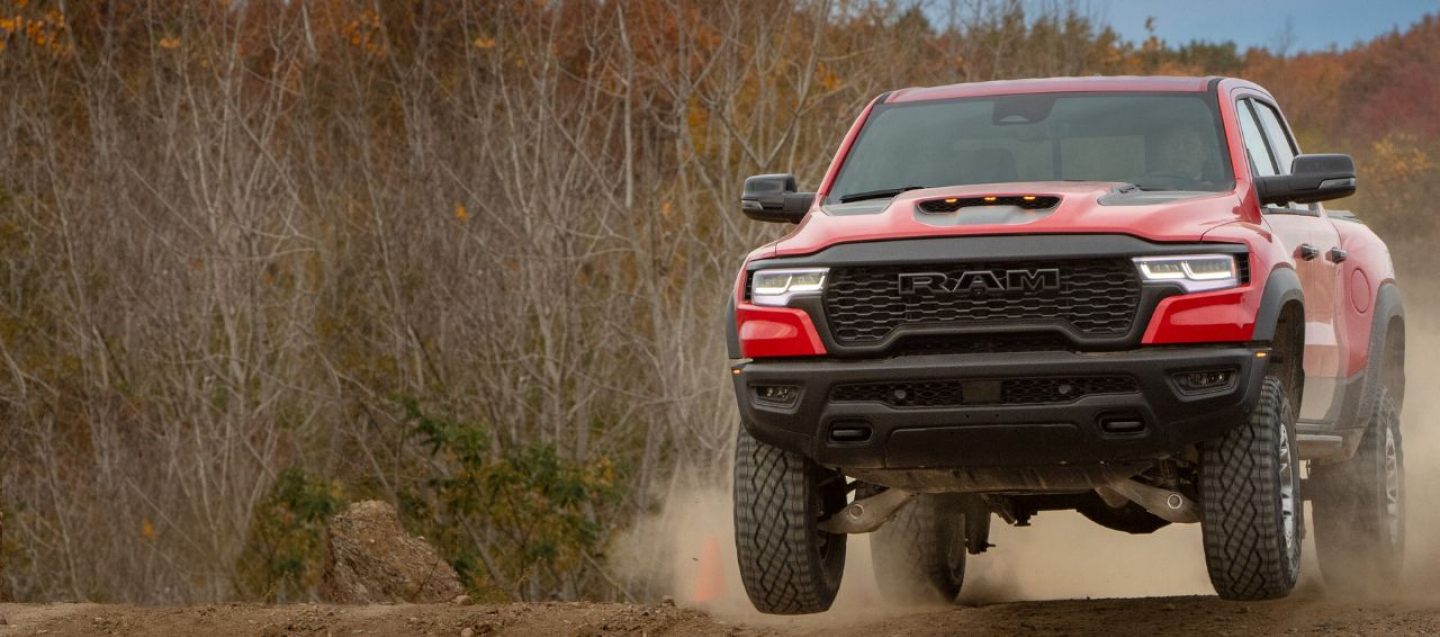 A head-on angle of a white 2025 Ram 1500 Big Horn 4x4 Crew Cab being driven up a curved mountain road in the desert. It's Ram Season.